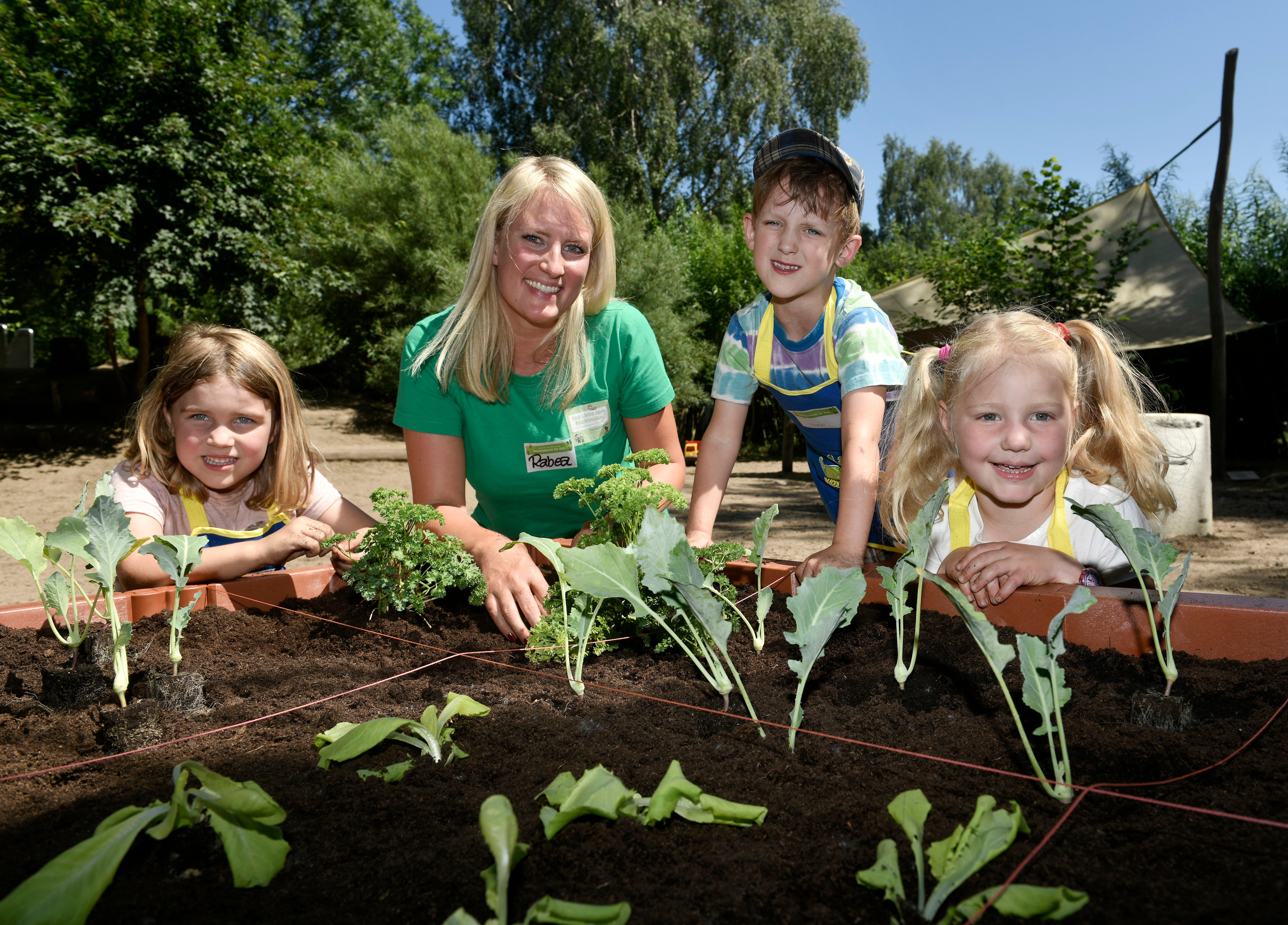 Mehrere Kita-Kinder und ein Teamitglied der EDEKA Stiftung stehen am Hochbeet von "Gemüsebeete für Kids" der EDEKA Stiftung.