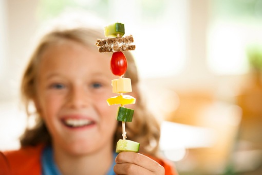 Ein Junge hält lachend einen Paratenspieß in die Höhe, dies ist das aufgespiesste Frühstück am Projekttag.