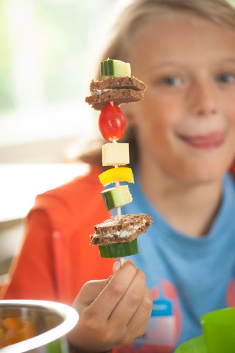 Ein Schüler hält zum Frühstück einen Piratenspieß hoch beim Projekttag "Mehr bewegen - besser essen" der EDEKA Stiftung.